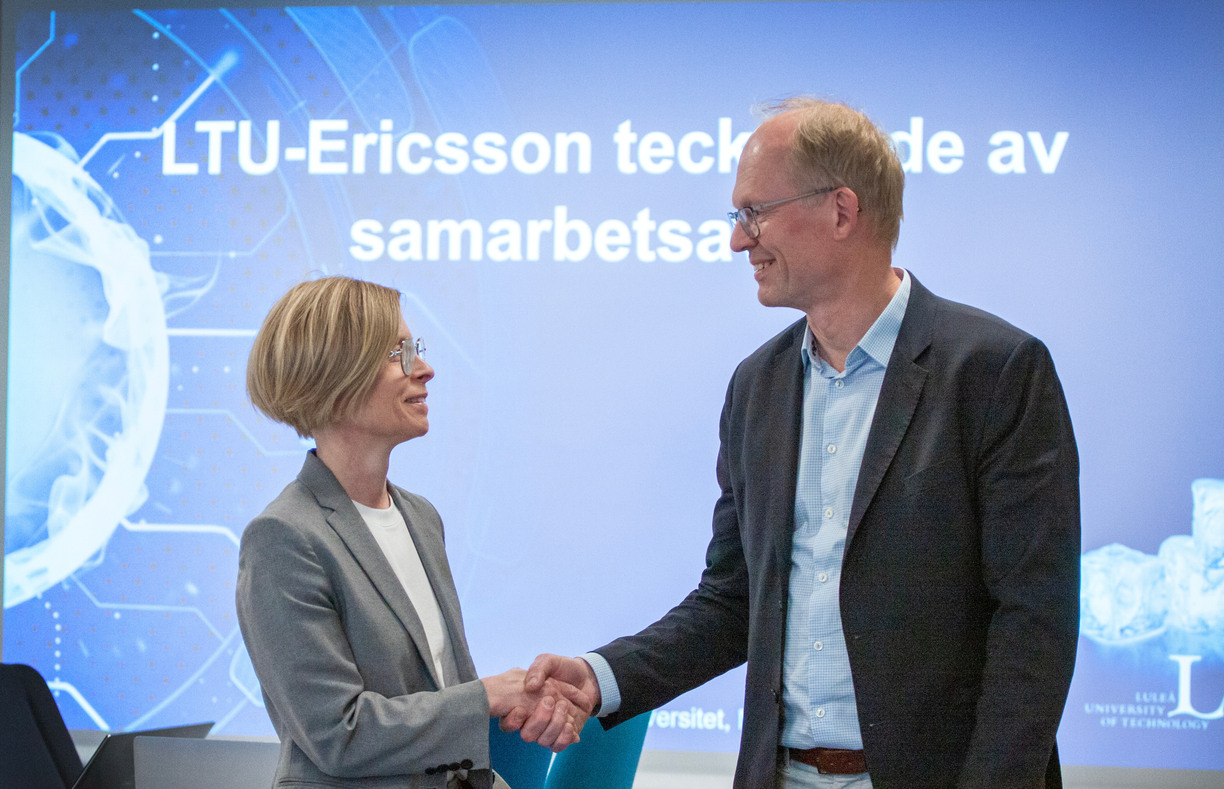Birgitta Bergvall-Kåreborn, Vice_Chancellor at Luleå University of Technology and Magnus Frodigh, Vice-President and Head of Ericsson Research shake hands and look at each other in the background of a presentation