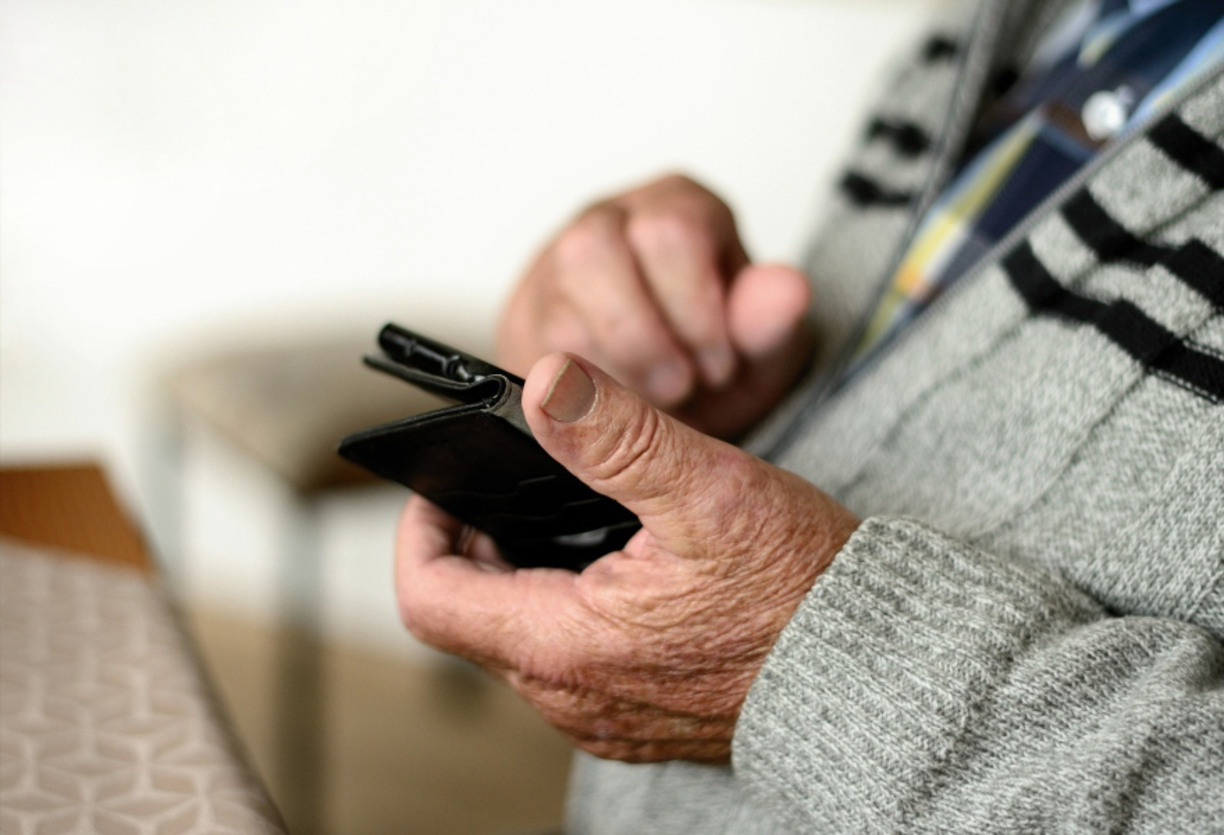 Närbild på en äldre persons händer som håller i en mobiltelefon