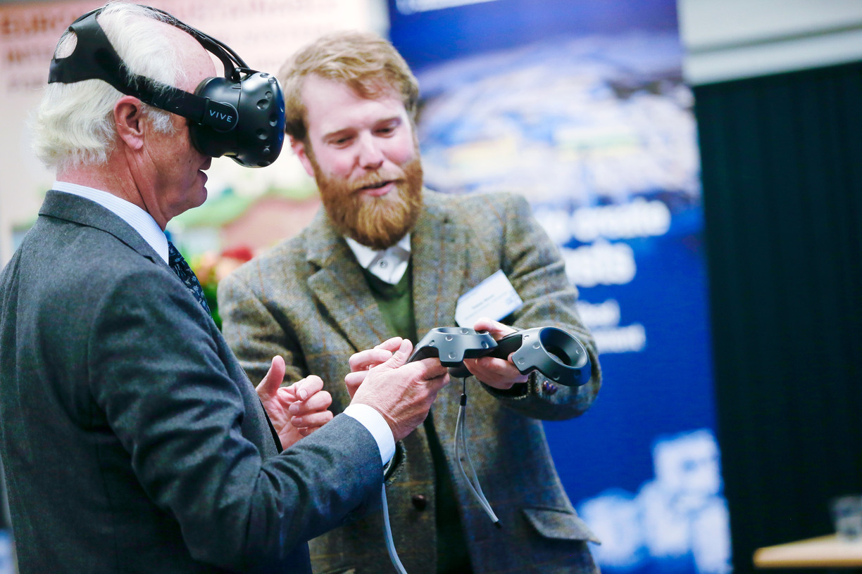 The king, wearing VR-glasses, being handed controllers by Tobias Bauer