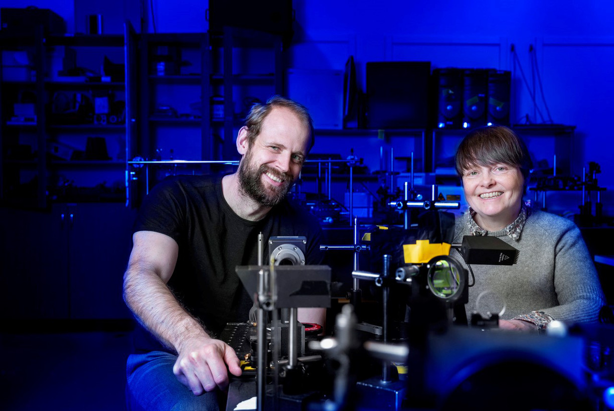 Joel Wahl och Kerstin Ramser sitter i ett nedsläckt labb intill mikroskop leende in i kameran