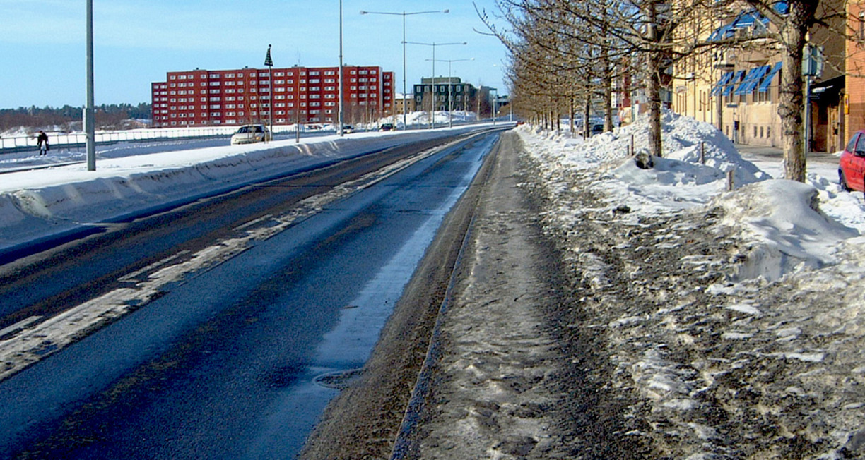 Till vänster syns en väg samt röda höghus långt bort. Till vänster smustig snö.