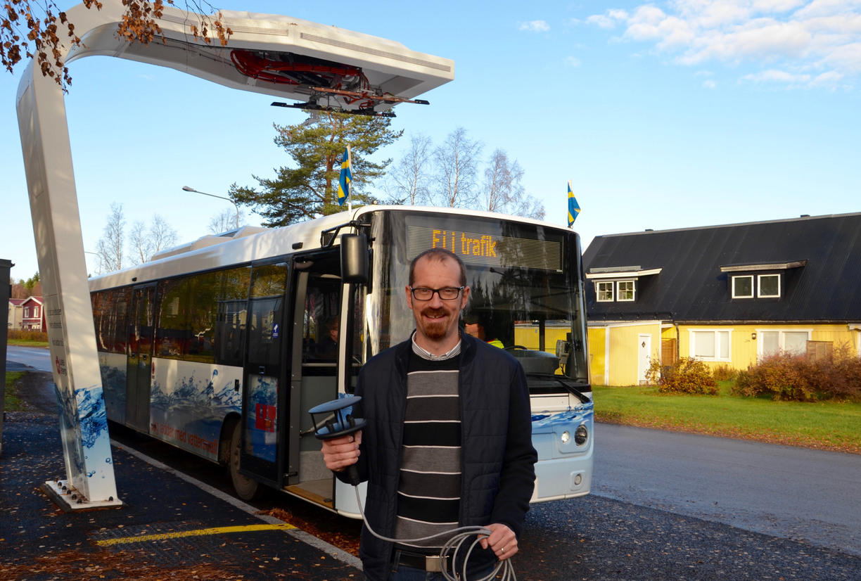 Johan Casselgren holding a weather station, in front of a bus by a bus stop