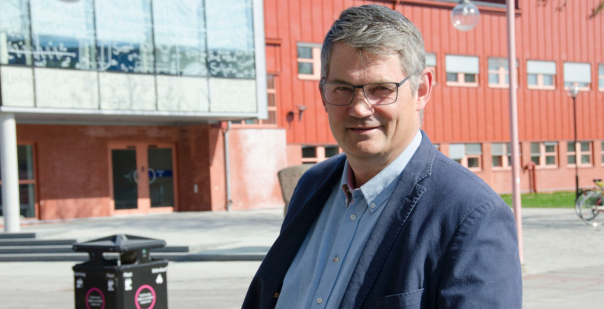 Jan-Olov Johansson ler in i kameran, i bakgrunden en röd byggnad