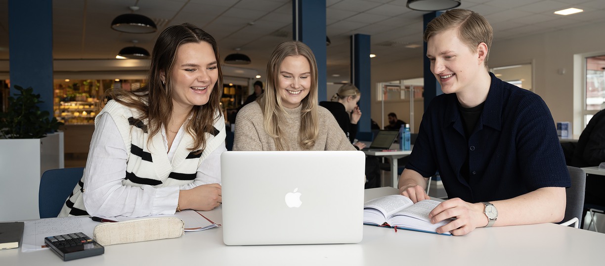 Två unga kvinnor och en ung man tittar på en datorskärm och ler