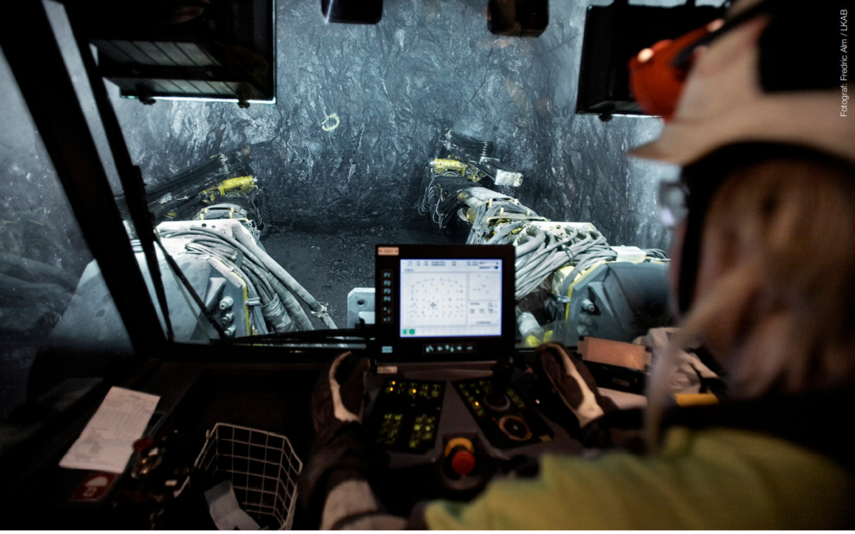 A mining machine operated by a person in protective gear, seen from within the machine