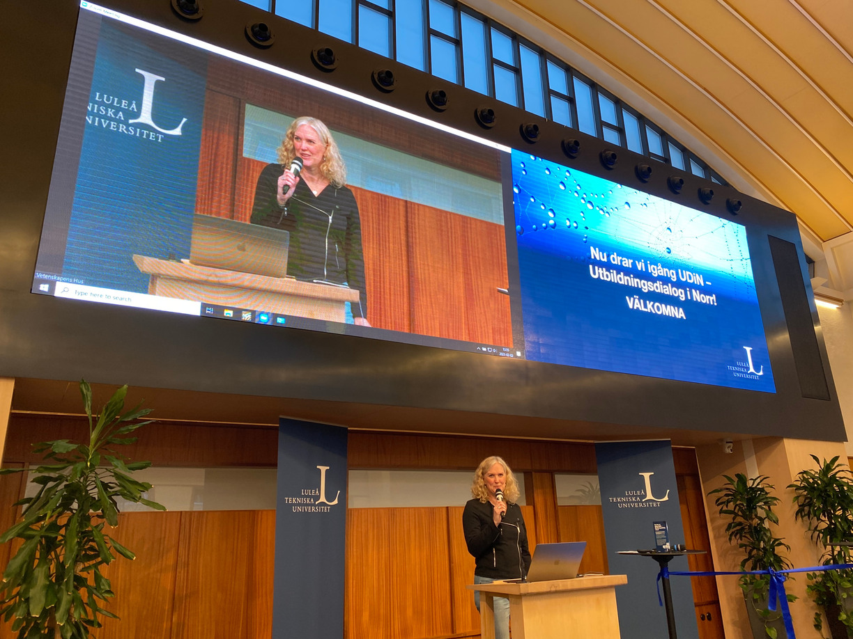 Ulrika Bergmark presents on stage in Vetenskapen hus, with a screen and presentation in the background