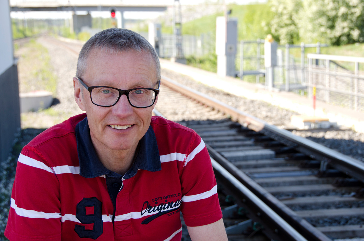 Bjarne Bergquist tittar in i kameran och ler i bakgrunden syns en järnväg