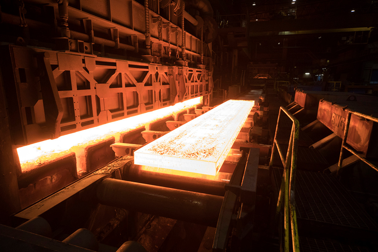 Red hot slab of steel undergoes hot rolling inside factory