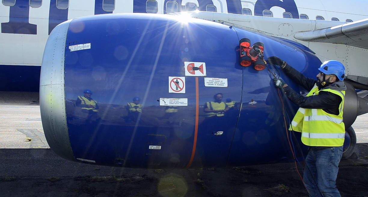 En man i reflexväst och skyddshjälm arbetar vid en flygplansturbin