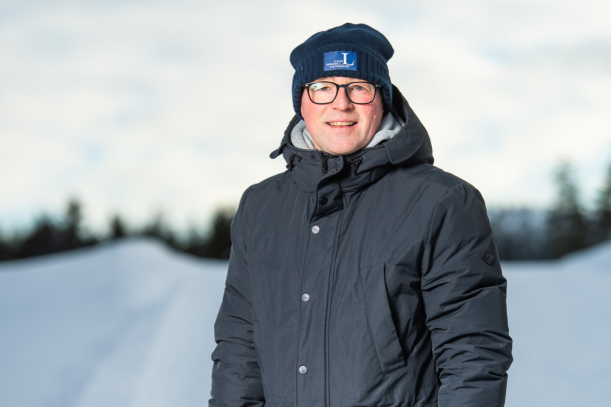 Joakim Abrahamsson ler in i kameran står utomhus med snö och träd i bakgrunden