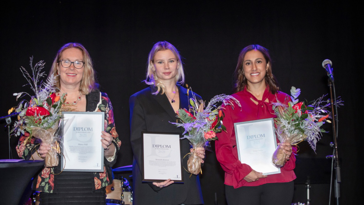 Maria Häll, Amanda Jansson and Shilpi Sinha stand on stage next to a microphone, all holding diplomas and a bouquet of flowers