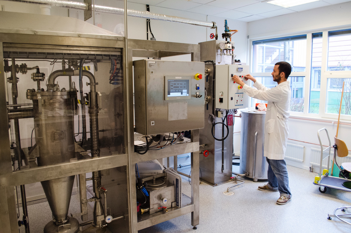 Maskin i kemiskt laboratorium. Till höger en man i vit labbrock.